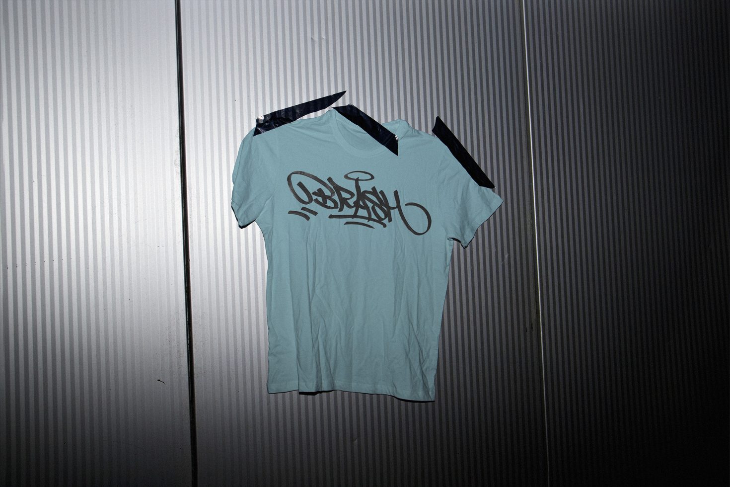 T-shirt mockup with graffiti design on a corrugated metal backdrop ideal for urban clothing presentation for designers.